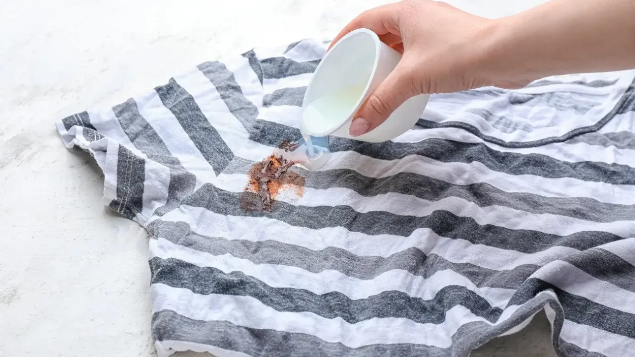 Jak usunąć plamy z czekolady? Płynny środek wylewany na brudny, pasiasty t-shirt.