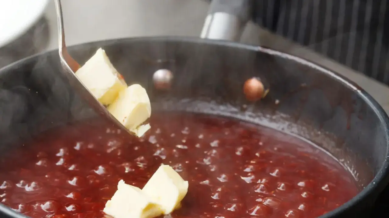 Butterstücke werden in eine köchelnde rote Sauce gegeben, um sie zu **saucen andicken** und zu verfeinern.