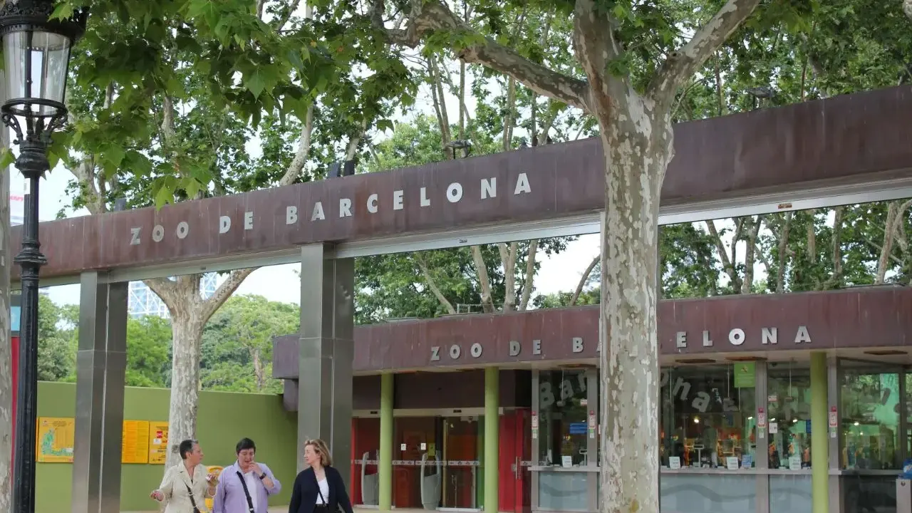 Eingang zum Zoo de Barcelona mit drei Frauen, die davor spazieren gehen.
