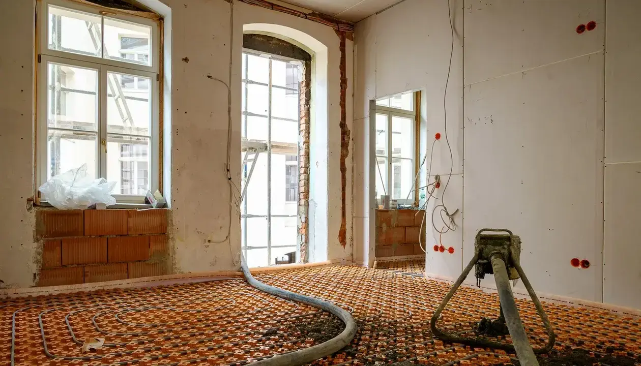 Installation d'un chauffage au sol ancienne génération, avec tuyaux orange et une machine de projection de chape.