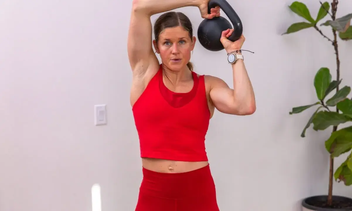 Frau trainiert mit einer Kettlebell deutsch, hebt sie über den Kopf.