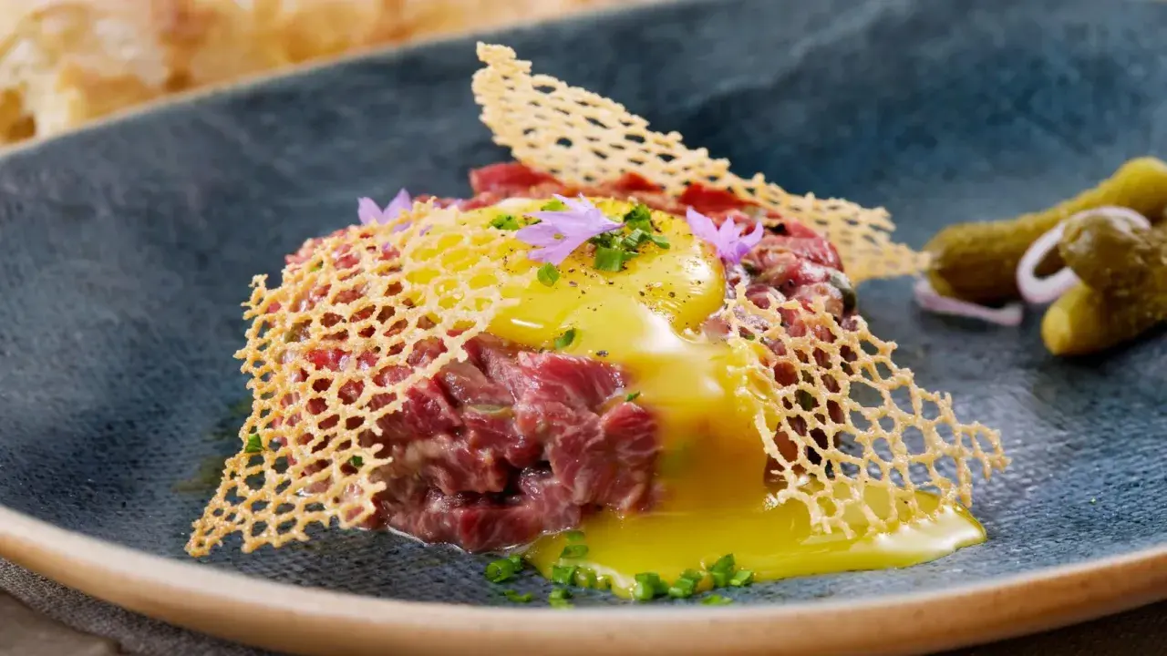 Delicioso steak tartar con huevo crudo, crujiente de queso y pepinillos. Una receta para disfrutar.