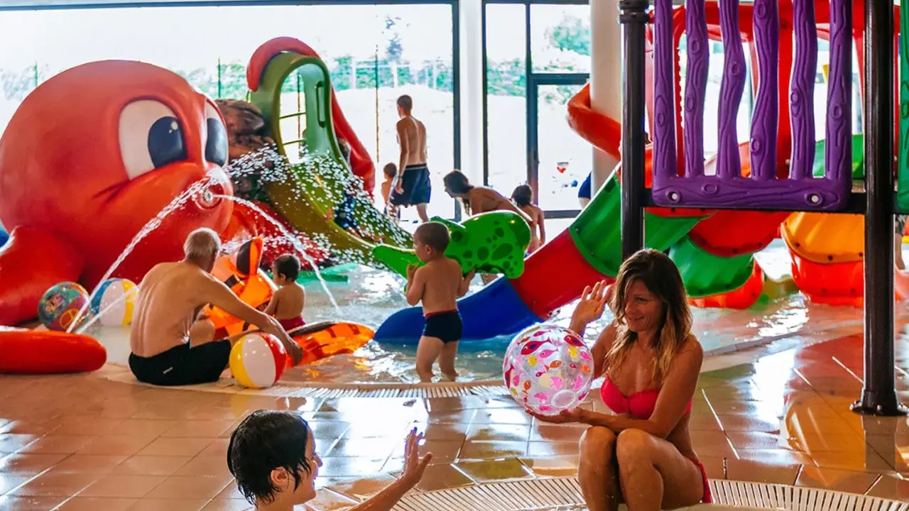 Bambini e adulti si divertono nelle **terme per bambini** con scivoli colorati e una grande attrazione a forma di polpo che spruzza acqua.