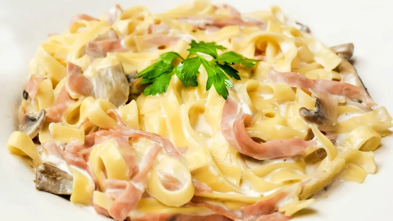 Tagliatelle z szynką i pieczarkami w kremowym sosie, ozdobione natką pietruszki. Pyszny makaron z mozzarellą w roli głównej.