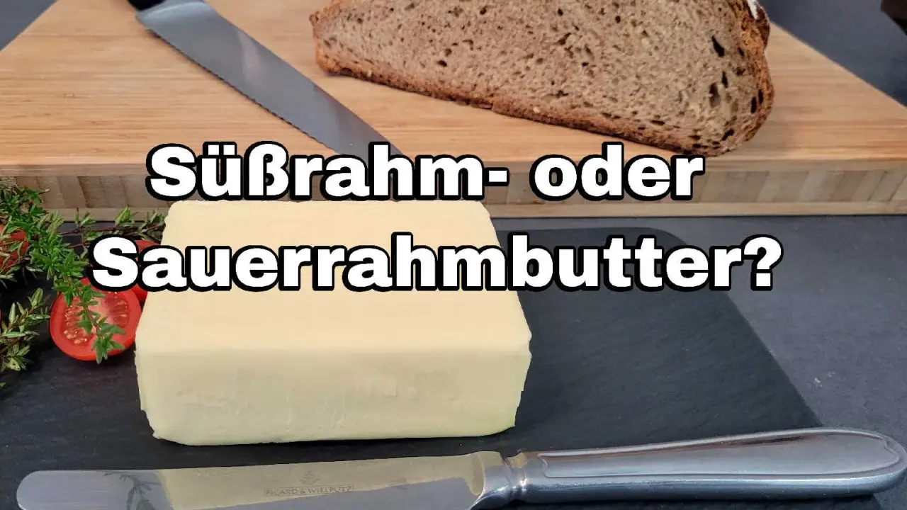 Ein Block Butter liegt neben Brot und Kräutern. Die Frage: Süßrahm- oder Sauermilchbutter?