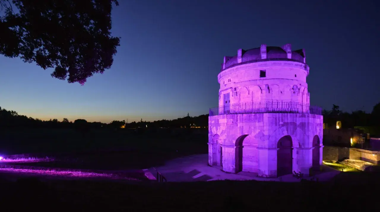 Torre antica illuminata di viola in una magica pink night. L'erba e gli alberi riflettono la luce, creando un'atmosfera surreale.