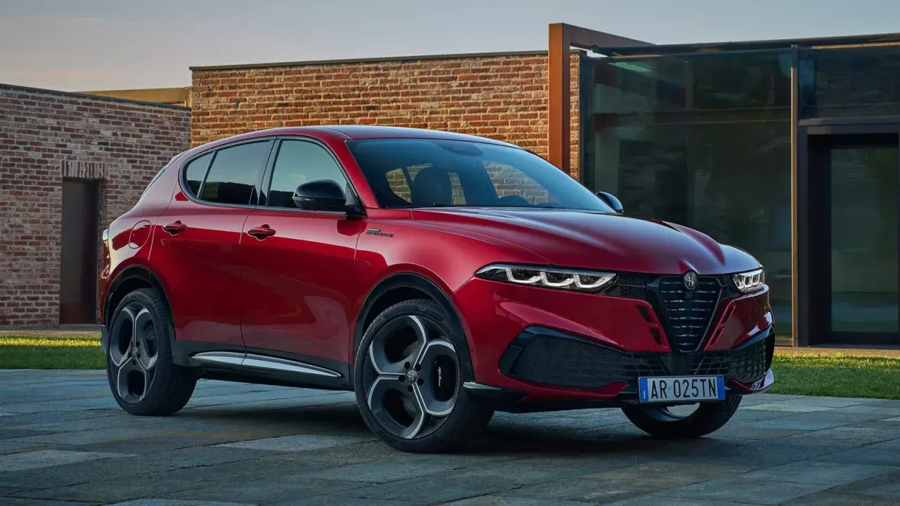 Czerwone Alfa Romeo Tonale na tle nowoczesnej architektury. Sprawdź aktualną alfa romeo tonale cena i konfigurację.