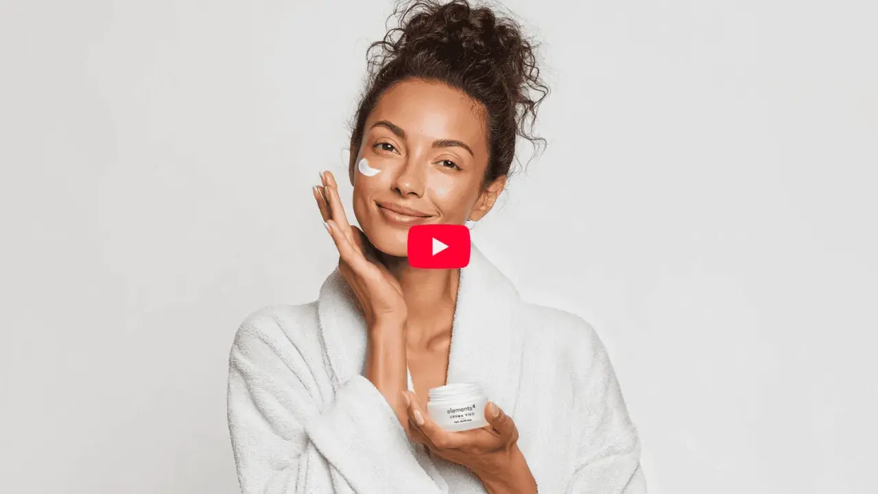 Donna sorridente applica crema viso, un gesto di skincare semplice per una pelle radiosa.