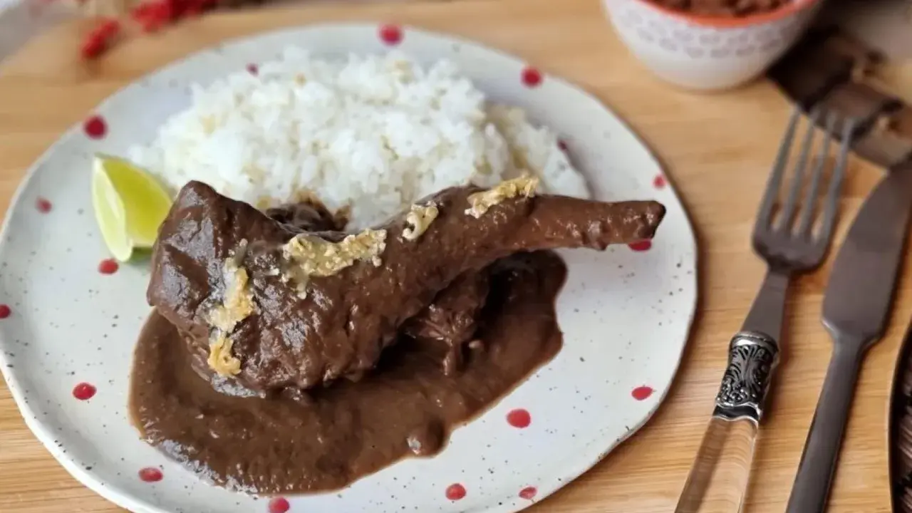 Un delicioso conejo guisado en mole oscuro, servido con arroz blanco y una rodaja de limón.