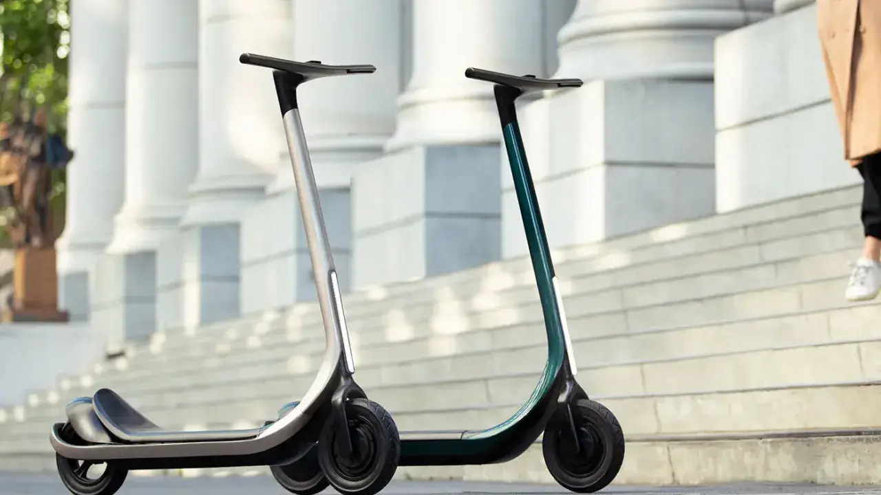 Deux trottinettes électriques modernes, idéales pour votre application trajet trottinette. L'une argentée, l'autre vert émeraude, sur des marches devant des colonnes.