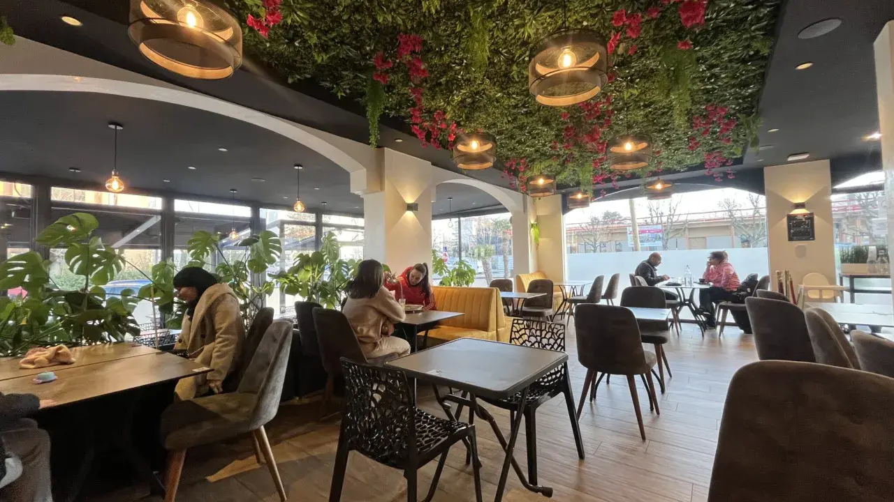 Intérieur d'un bar à desserts avec plafond végétalisée, lumières suspendues et tables occupées.
