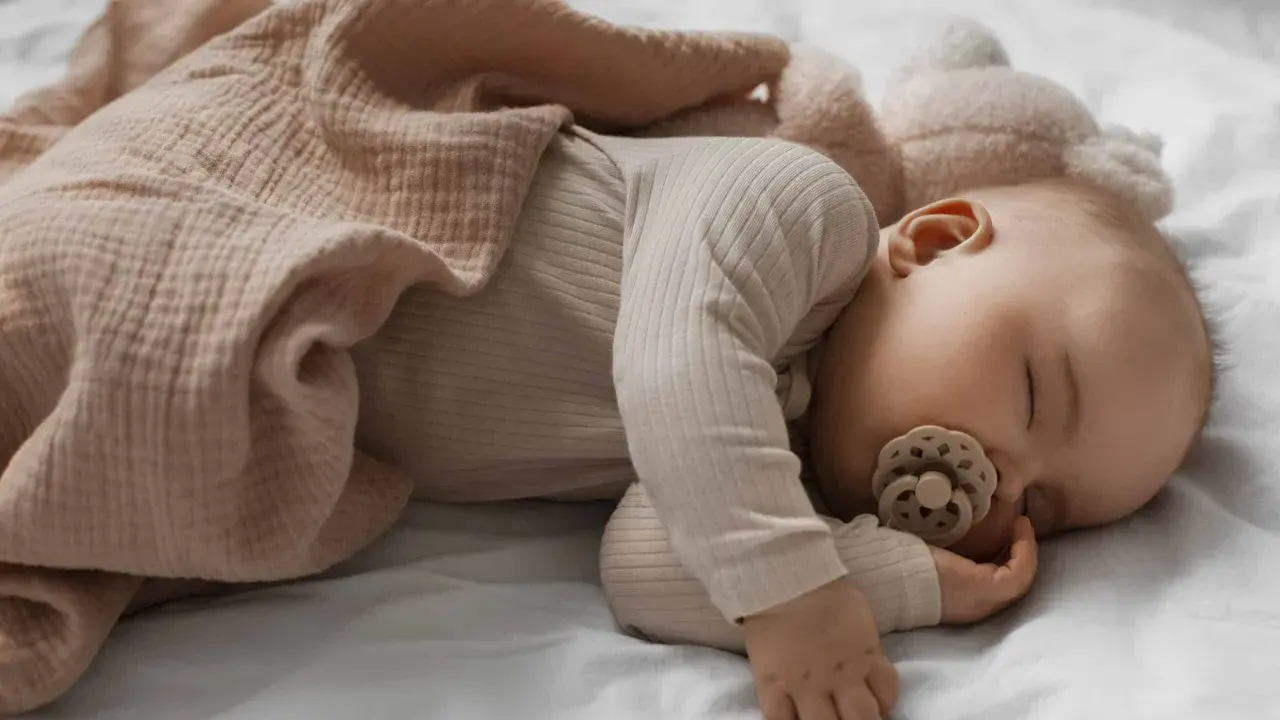 Dolce neonato di 3 mesi dorme sereno, avvolto in una copertina rosa cipria, con un ciuccio in bocca.