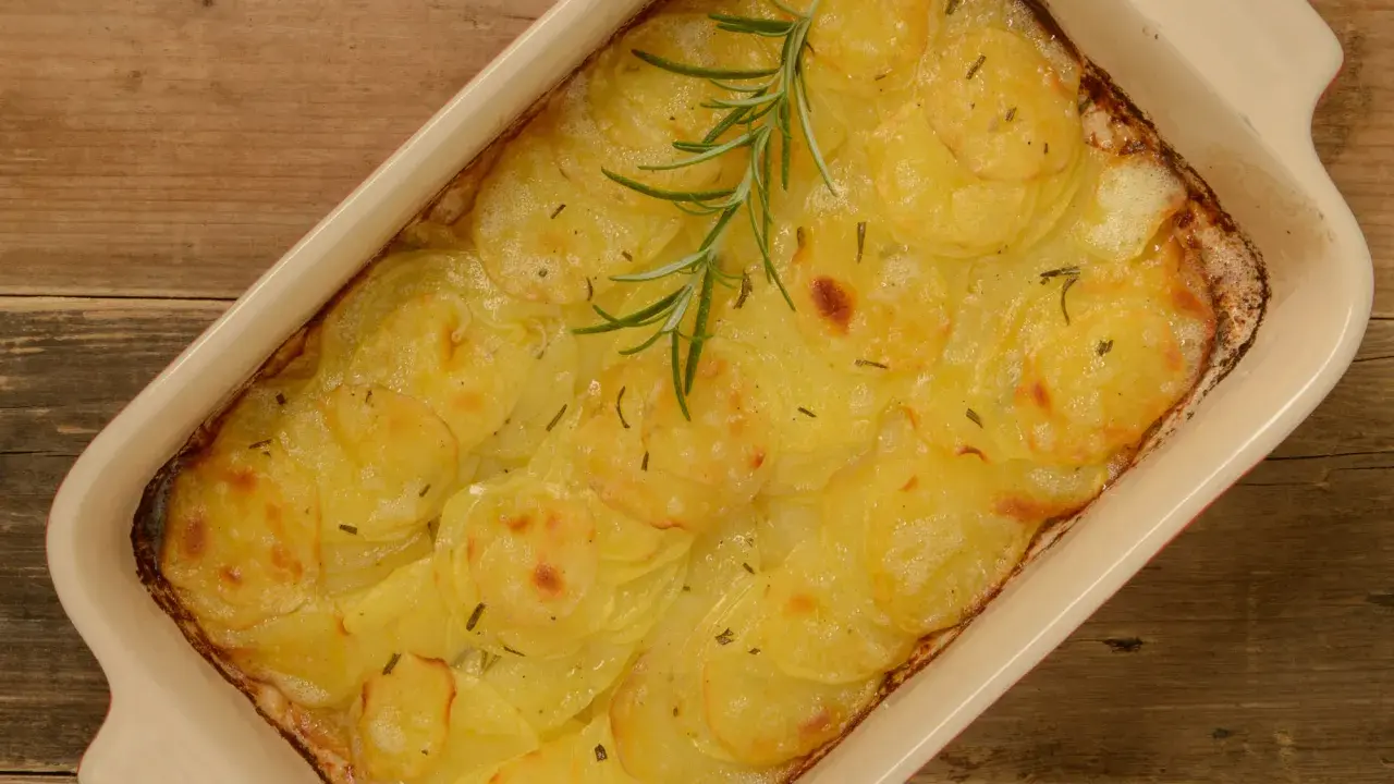En ugnsform med gyllene, tunna potatisskivor, en klassisk pommes anna, toppad med en rosmarinkvist.