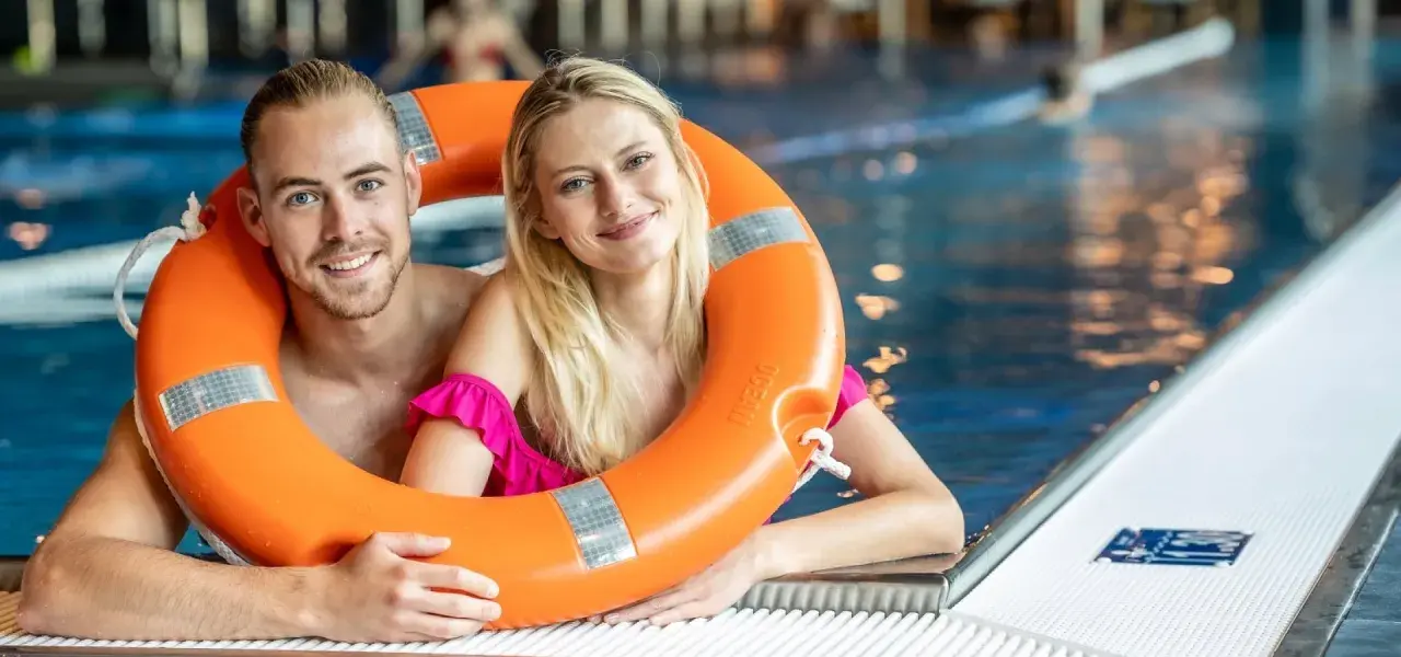 Uśmiechnięta para w basenie, trzymająca koło ratunkowe. Idealny weekend z przyjaciółką, pełen relaksu i zabawy w wodzie.