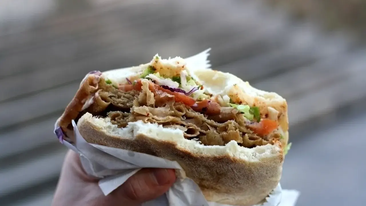 Ręka trzyma pysznego kebaba z mięsem, warzywami i chrupiącą surówką do kebaba.