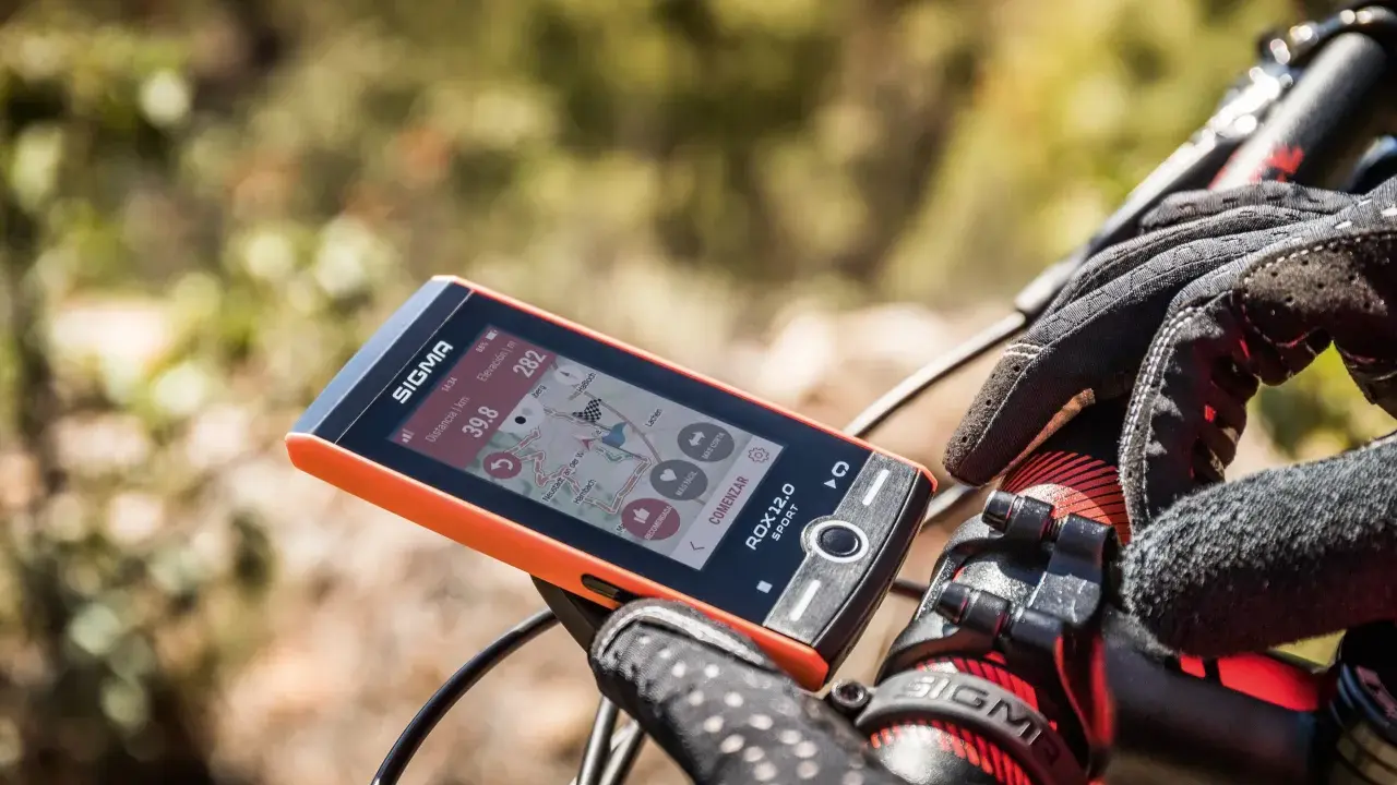 Pomarańczowy licznik rowerowy Sigma ROX 12.0 Sport pokazuje dystans 39.8 km i wysokość 282 m. Rękawiczka rowerowa na kierownicy.