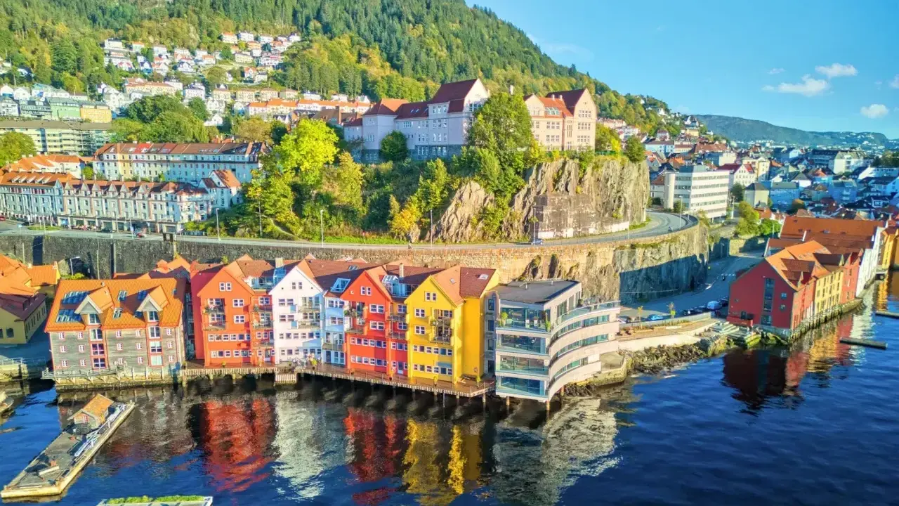 Kolorowe domy nad wodą w Bergen, idealne na norwegia zwiedzanie. W tle wzgórza porośnięte drzewami.