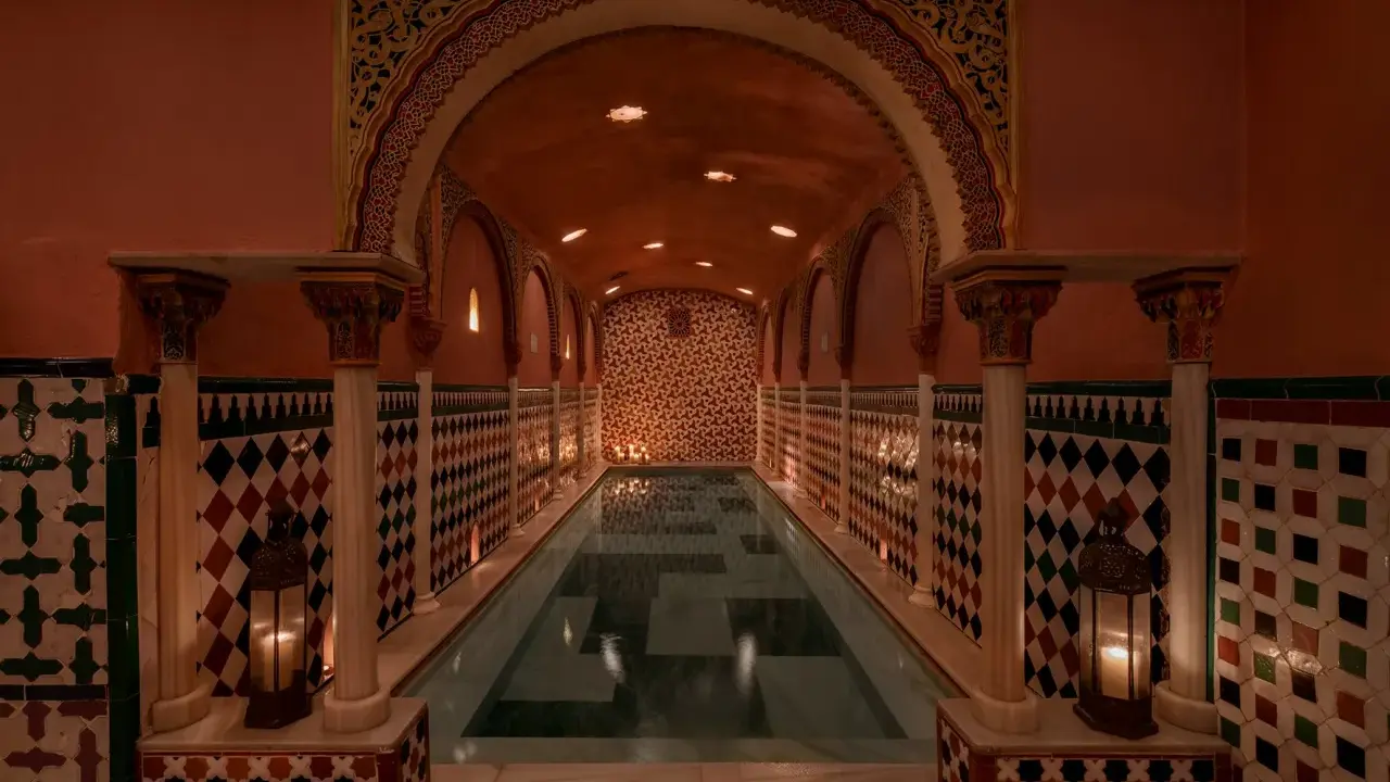 Ein prachtvoller Hammam in Granada mit einem langen Pool, umgeben von kunstvollen Kacheln und Säulen, beleuchtet von Kerzen.