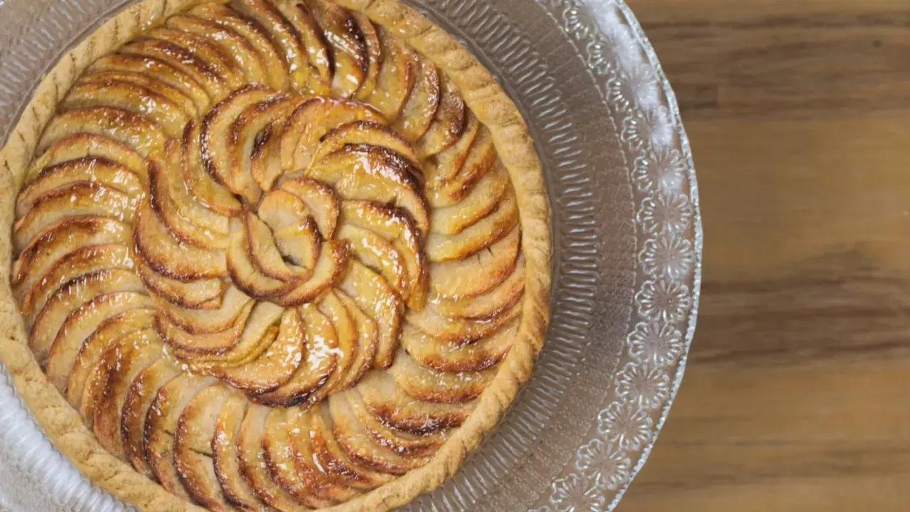 Tarte aux pommes dorée sur pâte feuilletée, disposée en spirale sur un plat en verre gravé. Un délice croustillant.