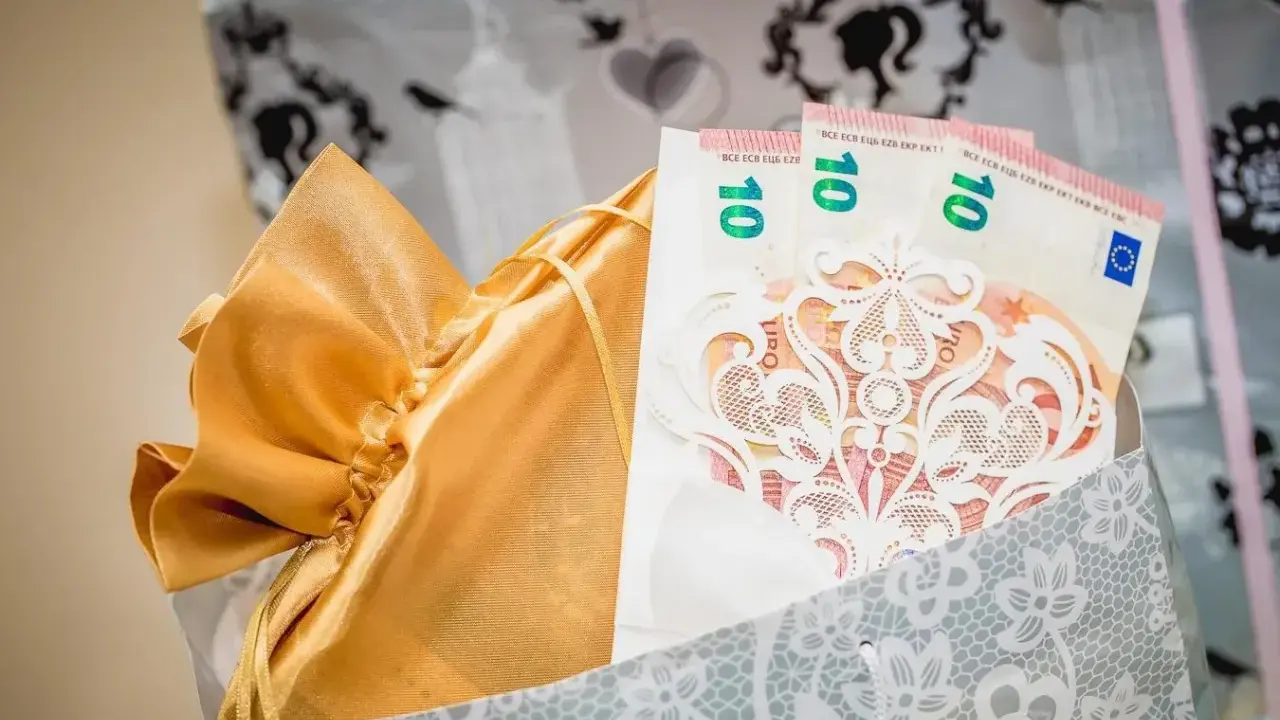 Elegancki sposób na to, jak zapakować pieniądze na ślub: banknoty 10 euro w ozdobnej kopercie, w złotej sakiewce, w ozdobnej torbie.
