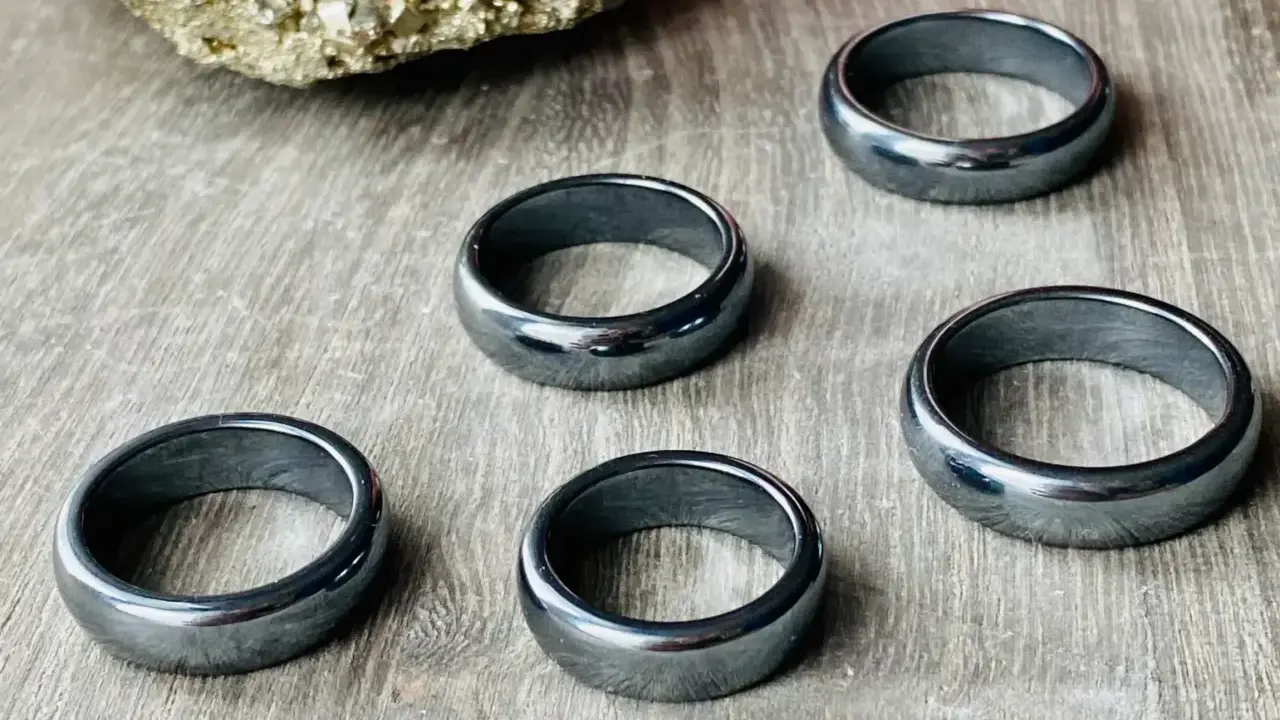 Pięć błyszczących, ciemnoszarych pierścionków z hematytu na drewnianym tle. Jak rozpoznać hematyt? Po jego metalicznym połysku i ciężarze.