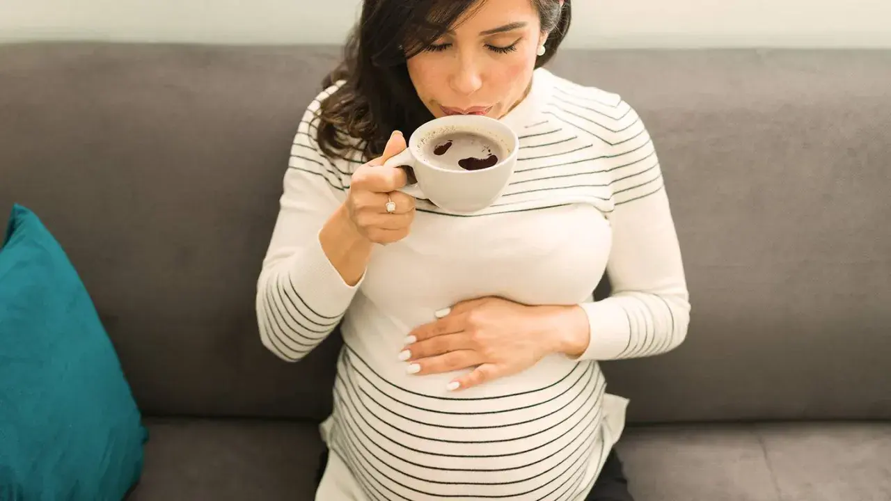 Schwangere Frau trinkt eine Tasse entkoffeinierten Kaffee, während sie ihren Bauch streichelt.