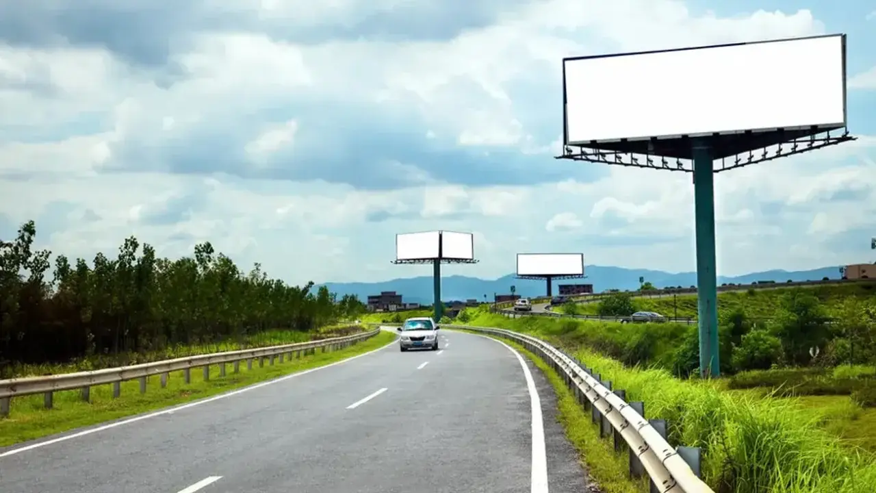 Pusta reklama przy drodze na terenie prywatnym, z widokiem na zakrzywioną autostradę i zielone wzgórza.