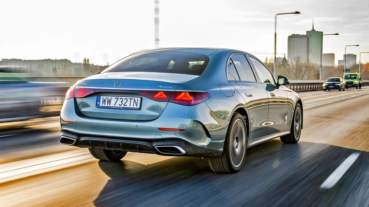 Elegancki, błękitny Mercedes E220d 4MATIC pędzi autostradą, mijając miejską panoramę.