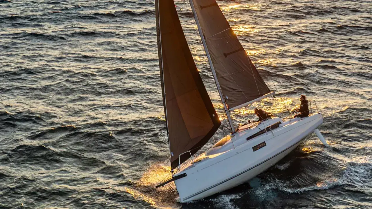 Voilier blanc naviguant sur une mer agitée au coucher du soleil. Les voiles sombres captent la lumière dorée. Idéal pour les premières 30 fiches techniques.