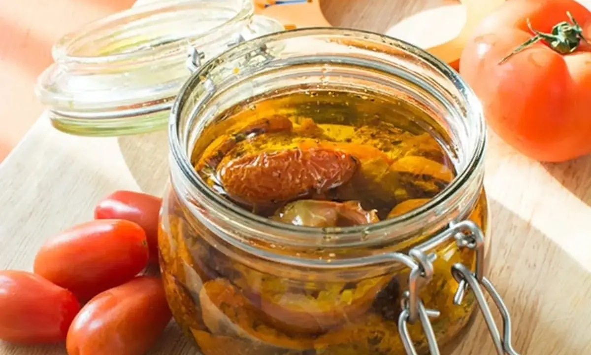 Bocal de tomates séchées à l'huile d'olive, avec des tomates fraîches à côté.