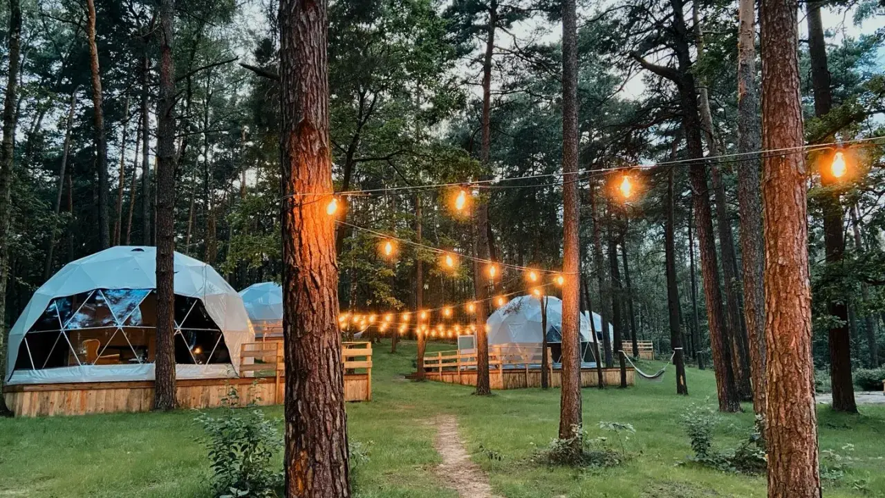 Nastrojowe **glamping w Polsce**. Kopuły mieszkalne w lesie, oświetlone girlandą żarówek.