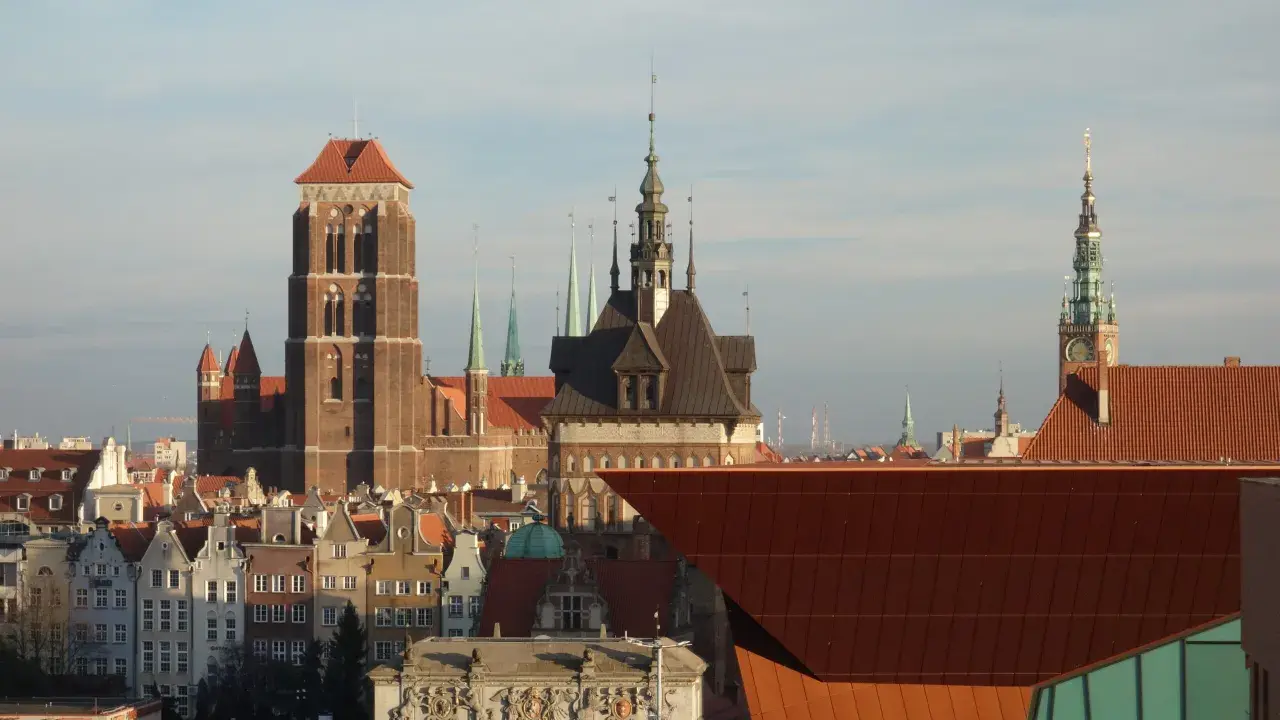 Gdańsk stare miasto z Bazyliką Mariacką i Ratuszem. Słońce oświetla zabytkowe kamienice i nowoczesną architekturę.