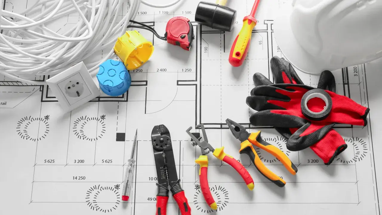 Outils d'électricien et rouleau de fil sur un plan architectural. Ce plan electrique maison détaille l'installation.