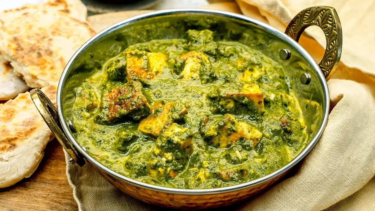 Ein köstliches Palak Paneer in einer traditionellen Schüssel, serviert mit Fladenbrot und Gewürzen.