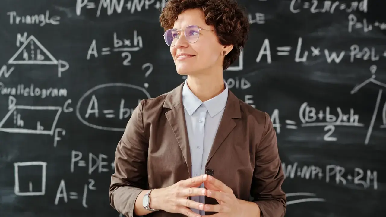 Lehrerin vor Tafel mit Matheformeln. Sie fragt sich, wie viel verdienen Grundschullehrer.
