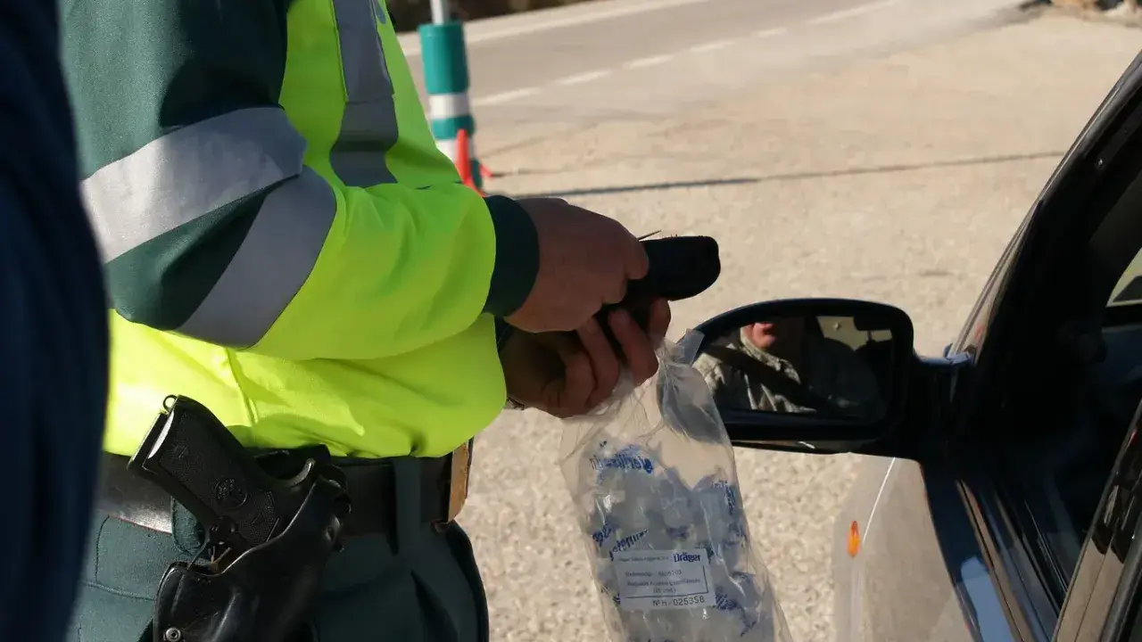 Policjant w kamizelce odblaskowej trzyma alkomat i worek z ustnikami przy samochodzie.