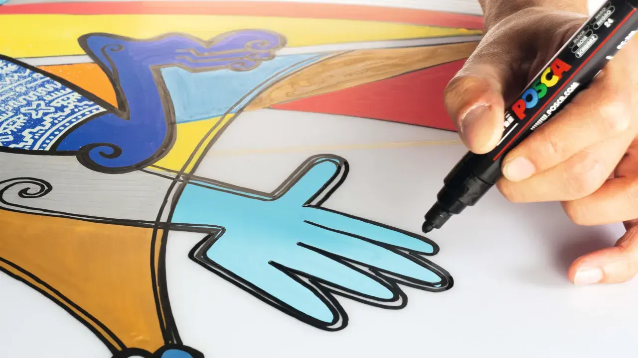 En hand använder en svart Posca-penna för att måla med posca pennor på en färgglad, abstrakt illustration.