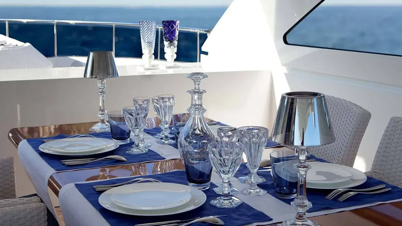 Emplacement des couverts sur une table dressée sur un yacht, avec des verres en cristal, une carafe et des lampes.