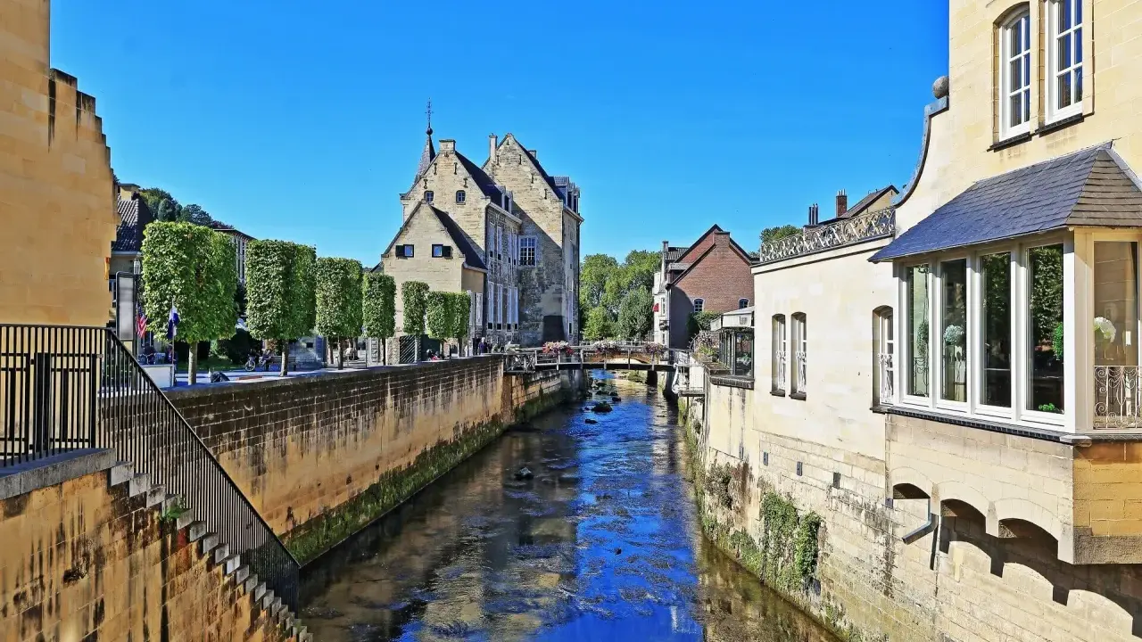 Idyllischer Kanal in der Valkenburg Altstadt, gesäumt von historischen Gebäuden und Bäumen.
