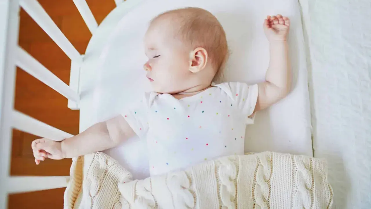 Baby schläft im Gitterbett, das Baby bewegt sich viel im Schlaf und streckt die Arme aus.