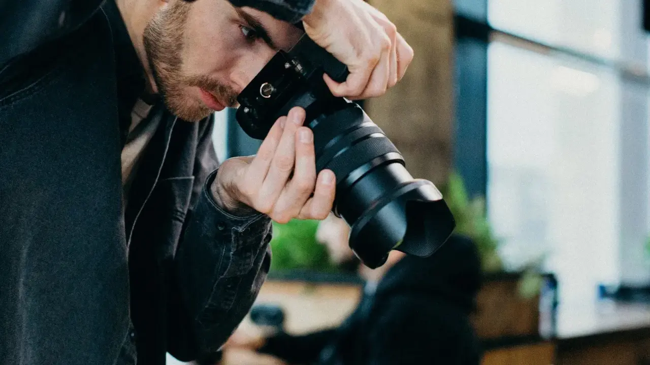 Mężczyzna z brodą w czarnej kurtce trzyma aparat, gotowy do uchwycenia chwili w stylu street photography.