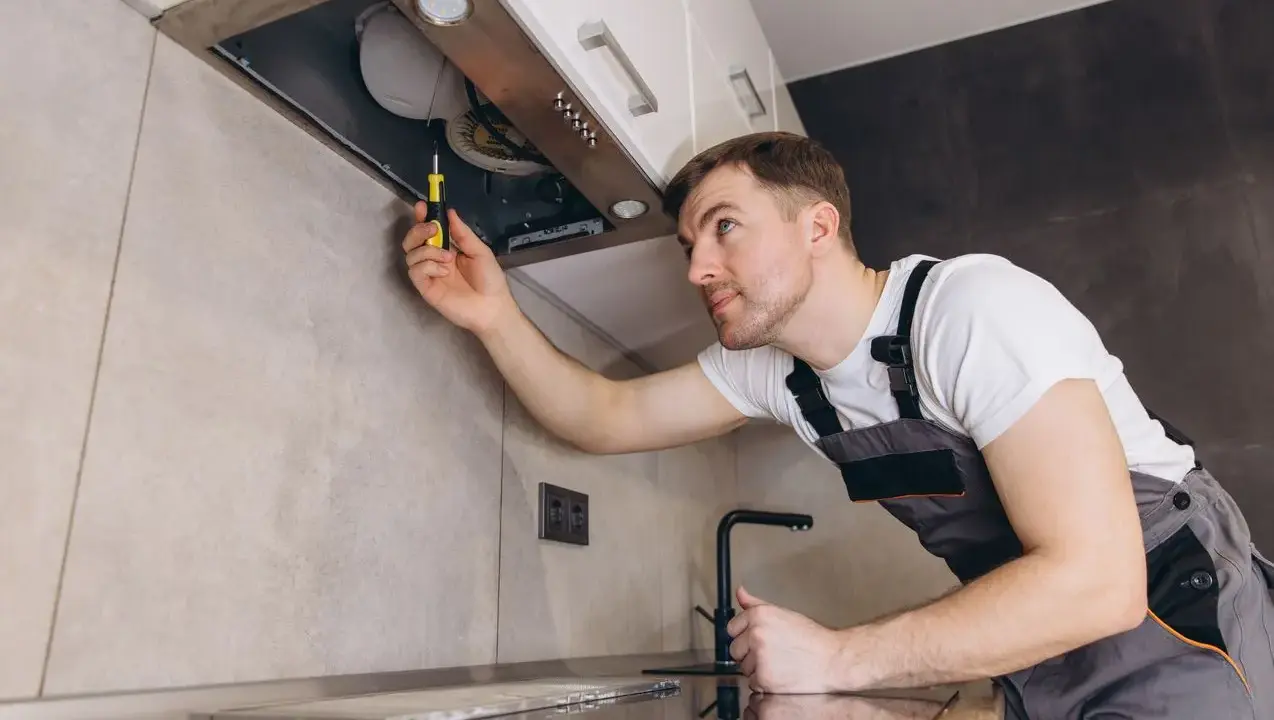 Un homme en salopette utilise un tournevis pour comment installer une hotte de cuisine.