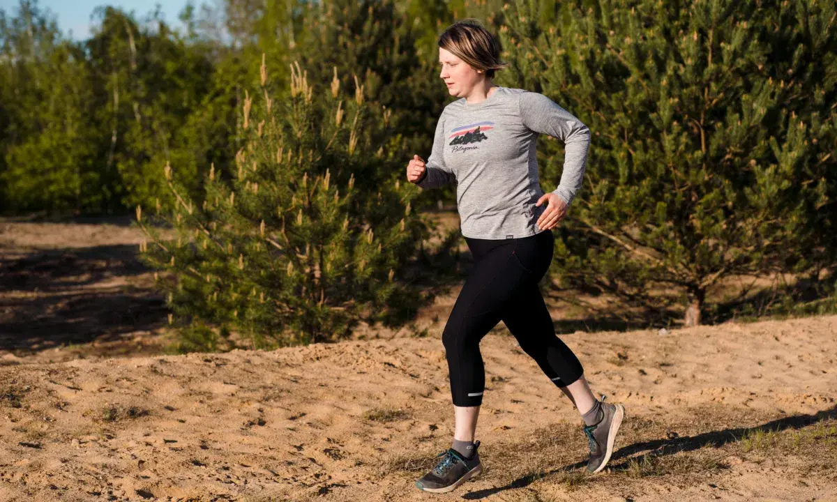 Frau beim **trail running** auf sandigem Untergrund, umgeben von Kiefern und Bäumen.