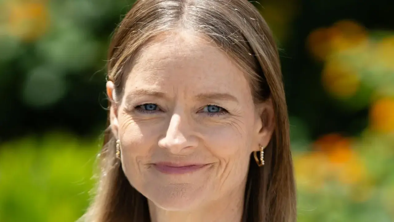 Porträt einer Frau mit blauen Augen und braunem Haar, das einige einzelne graue Haare abdeckt. Sie trägt goldene Ohrringe.