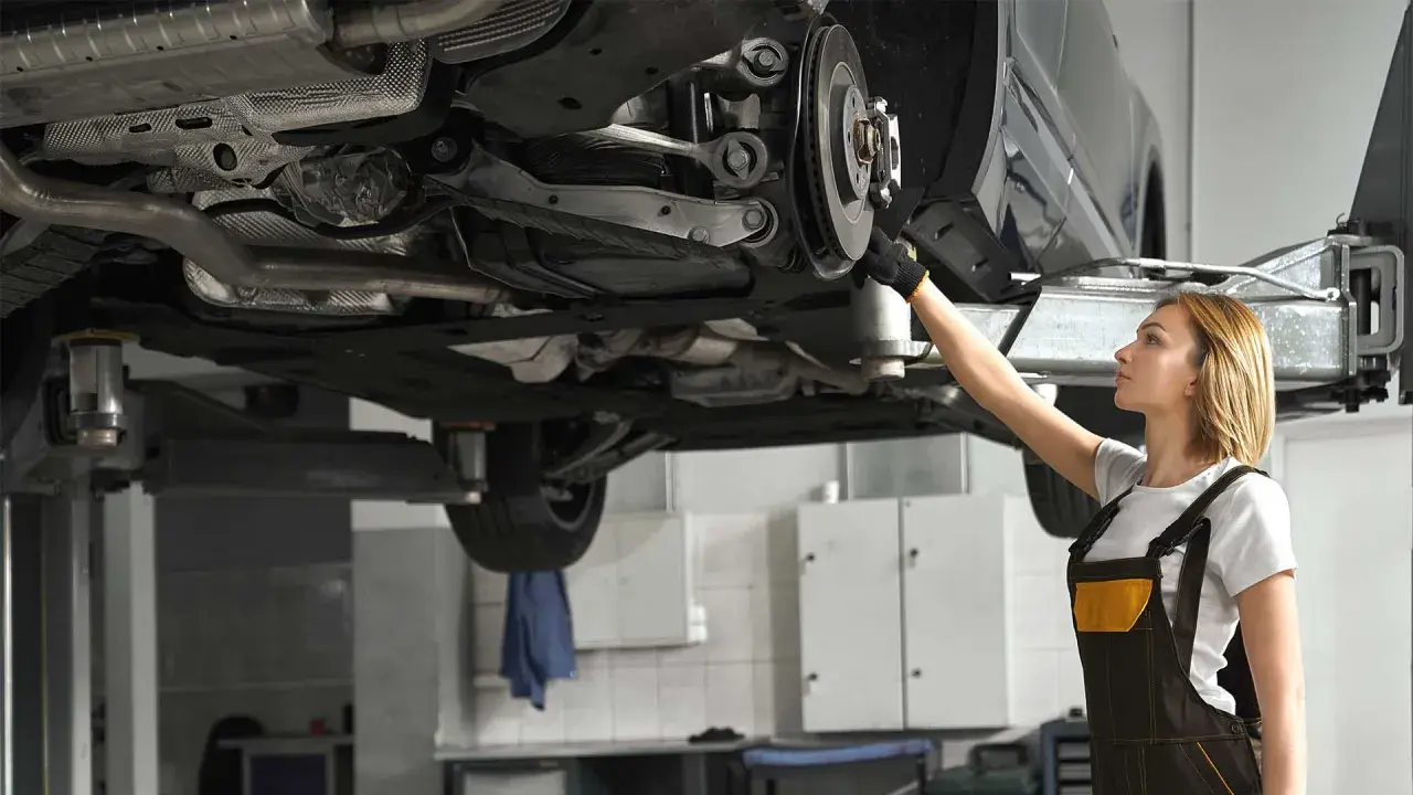 Mechaniczka sprawdza układ napędowy samochodu na podnośniku.