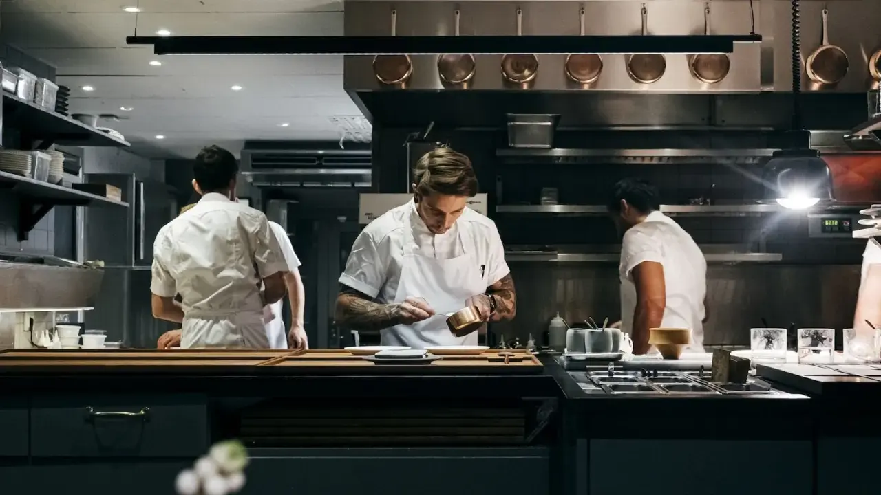 Chefs in a professional kitchen, one plating food.