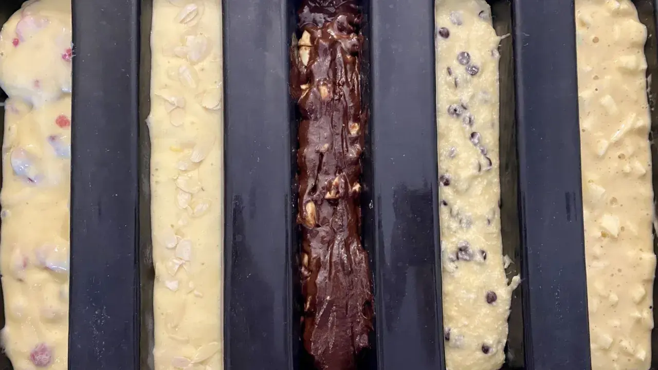 Cinq moules à cake longs prêts pour la cuisson : un aux fruits rouges, un aux amandes, un au chocolat, un aux pépites de chocolat et un aux pommes. Recette 5 cakes longs sucrés.
