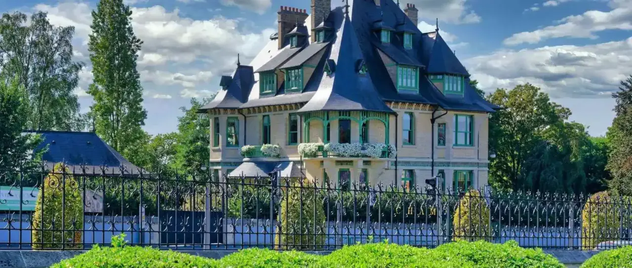 La villa Demoiselle à Reims, une demeure d'exception avec ses toits bleus et ses ornements verts, se dresse fièrement derrière une grille ouvragée.