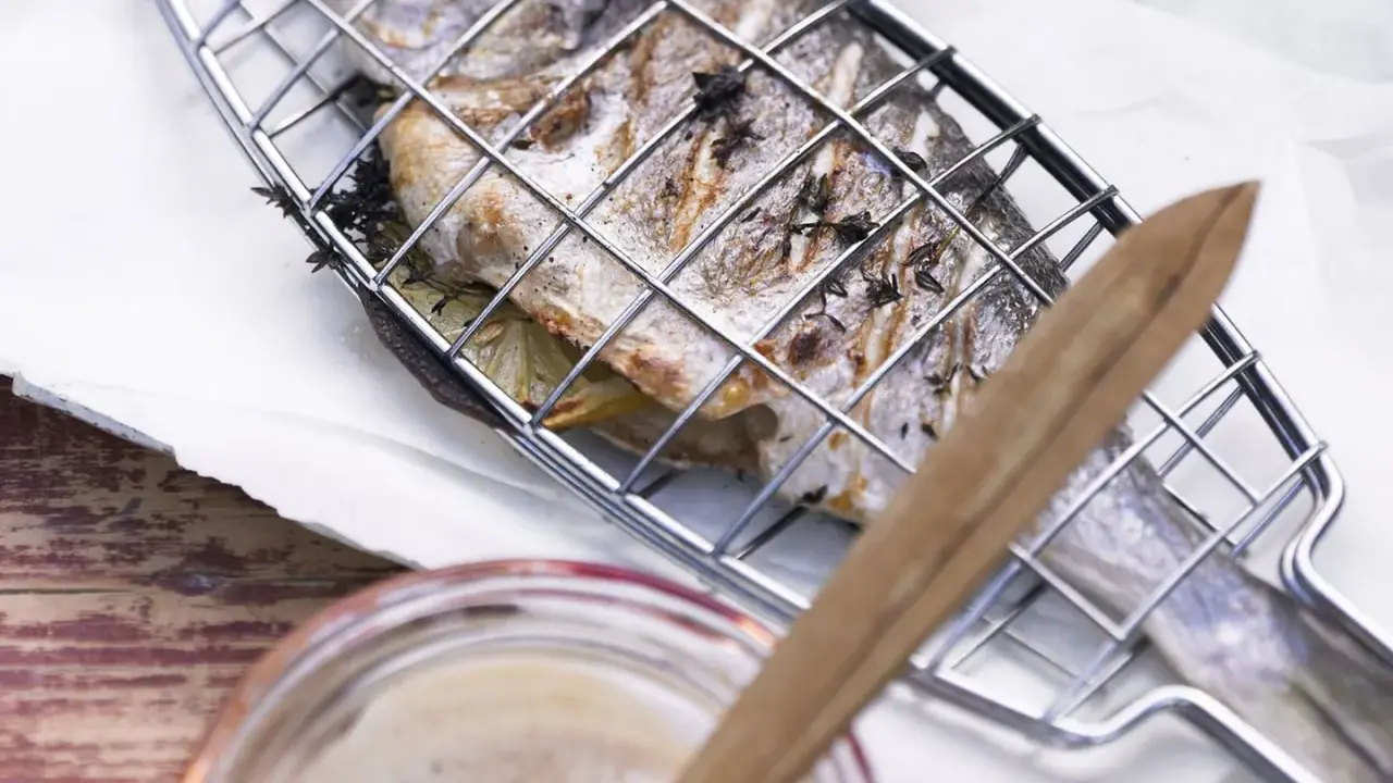 Ein ganzer Fisch liegt in einem Grillkorb, bereit zum Fisch grillen. Zitronenscheiben und Kräuter sind darin versteckt.