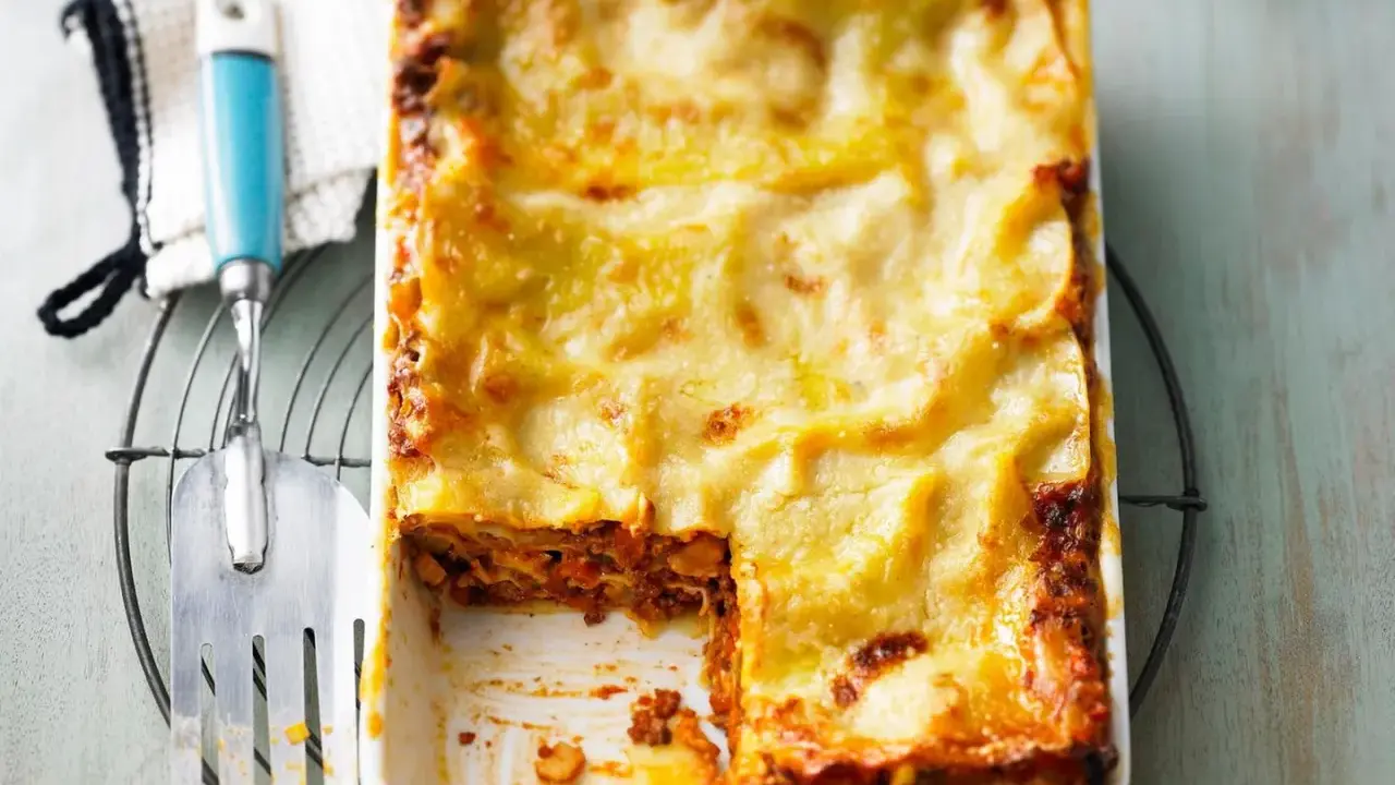 Eine frisch gebackene Lasagne al forno mit goldbraun überbackener Käseschicht, daneben ein Servierheber.